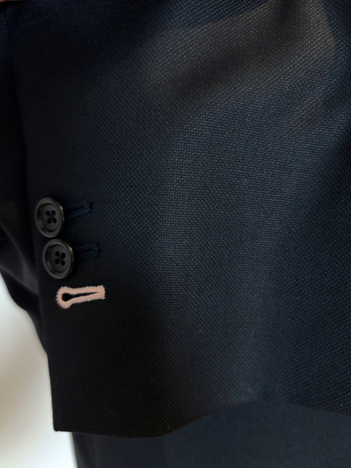 Close-up of a dark suit jacket with a button and embroidery detail.